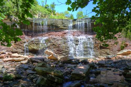 A serene waterfall cascading over rocky cliffs, surrounded by lush greenery and a clear stream below.