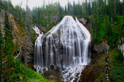 A majestic waterfall cascading down rocky cliffs, surrounded by lush green trees and a serene natural landscape.