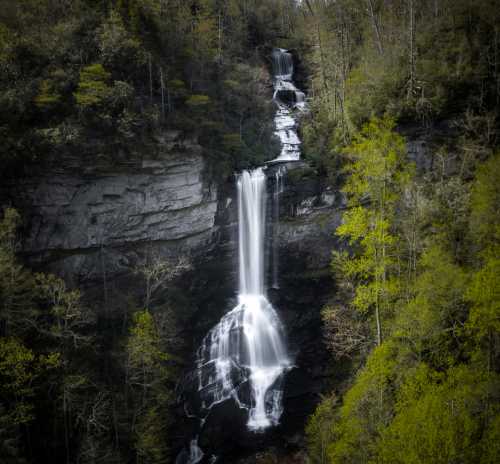 A stunning waterfall cascades down rocky cliffs, surrounded by lush green trees and vibrant foliage.