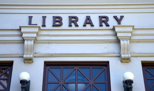 Sign on a building reading "LIBRARY," with decorative architectural elements and large windows below.