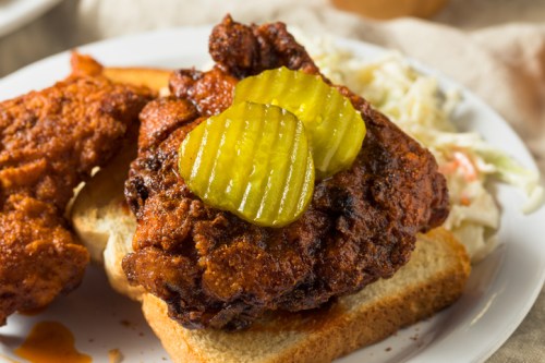 A plate featuring a fried chicken sandwich with pickles on bread, accompanied by coleslaw.