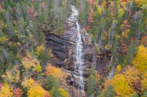 A cascading waterfall surrounded by vibrant autumn foliage in a forested landscape.