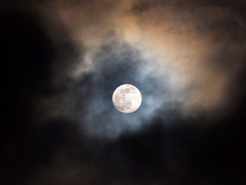 A bright full moon surrounded by dark, swirling clouds against a night sky.
