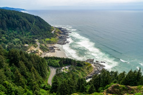 A scenic coastal view featuring lush green hills, rocky shores, and gentle waves along the ocean.