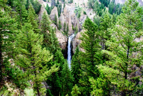 A waterfall cascades through a rocky canyon, surrounded by lush green trees and rugged cliffs.