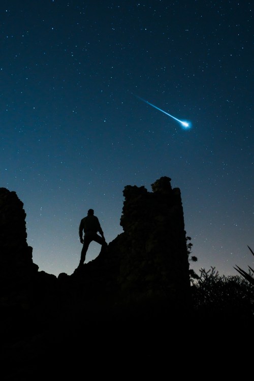 Silhouette of a person on ruins against a starry night sky with a bright comet streaking across.