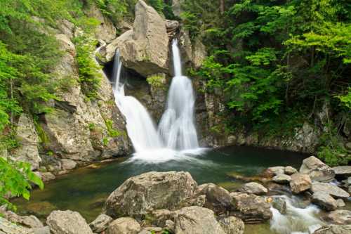 A serene waterfall cascades into a clear pool, surrounded by lush greenery and rocky terrain.