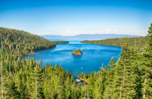 A scenic view of a lake surrounded by lush green forests and a small island, under a clear blue sky.