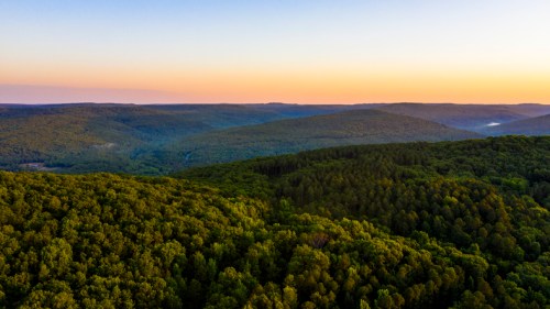 Aerial view of lush green hills and valleys at sunset, with soft light illuminating the landscape.