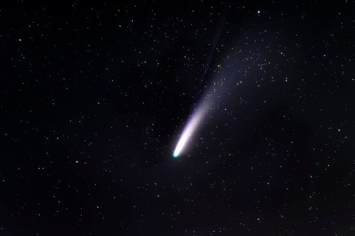 A bright comet with a glowing tail streaks across a star-filled night sky.