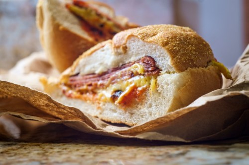 Close-up of a sandwich with layers of meat and melted cheese, resting on crumpled brown paper.