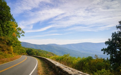 A winding road curves along a scenic mountain landscape under a blue sky with wispy clouds.