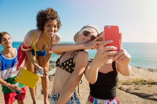 A group of friends taking a selfie at the beach, smiling and enjoying a sunny day by the ocean.