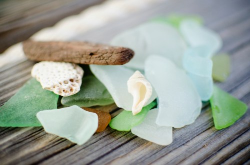 A collection of colorful sea glass pieces, shells, and driftwood on a weathered wooden surface.
