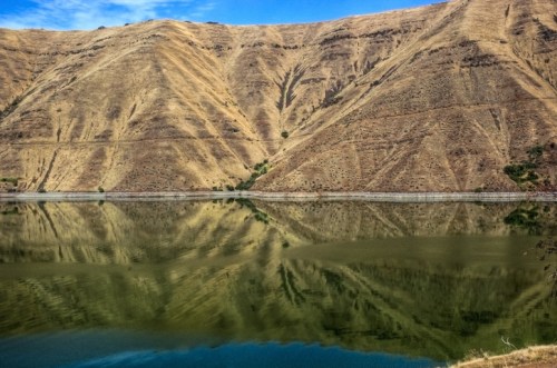 A serene lake reflecting golden hills under a blue sky, showcasing a tranquil natural landscape.