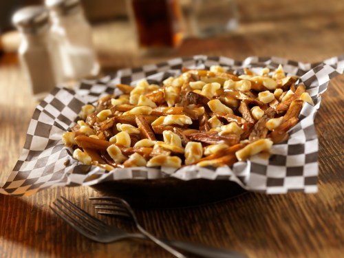 A plate of poutine with fries, cheese curds, and gravy, served on a checkered paper in a rustic setting.