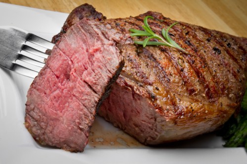 A perfectly cooked, juicy steak with grill marks, garnished with a sprig of rosemary, served on a white plate.