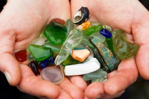 A pair of hands holding a colorful assortment of smooth, polished glass and stone pieces.