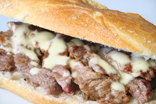 A close-up of a sandwich filled with sliced beef and drizzled with creamy sauce, served in a crusty bread roll.