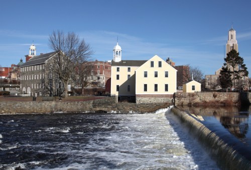 A scenic view of a river with a dam, flanked by historic buildings and a clear blue sky.