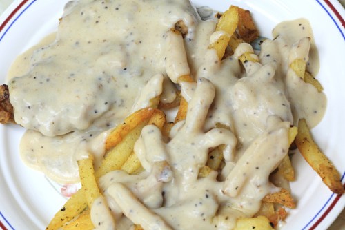 A plate of crispy fries topped with creamy gravy and two pieces of fried chicken smothered in sauce.