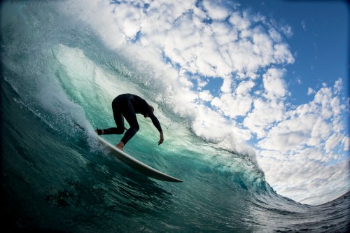 A surfer rides a large wave under a cloudy sky, showcasing dynamic movement and ocean energy.