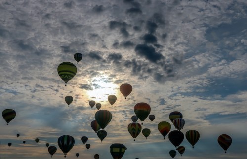 A sky filled with colorful hot air balloons against a backdrop of clouds and sunlight.