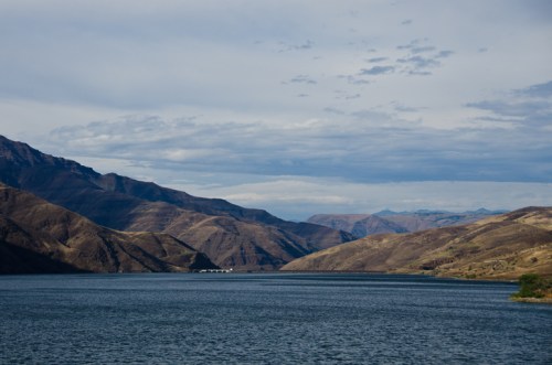 A serene lake surrounded by rolling hills and mountains under a cloudy sky.