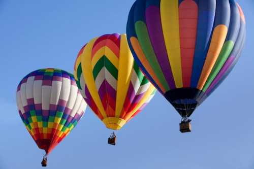 Three colorful hot air balloons floating against a clear blue sky.