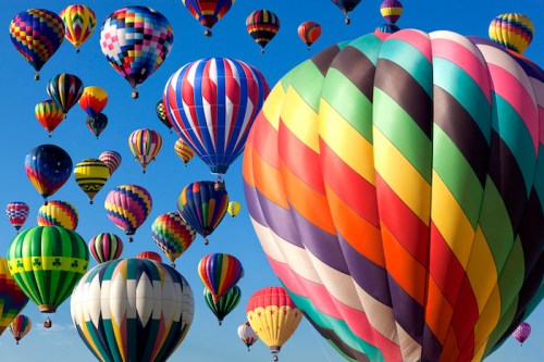 A vibrant sky filled with colorful hot air balloons of various patterns and designs against a clear blue background.