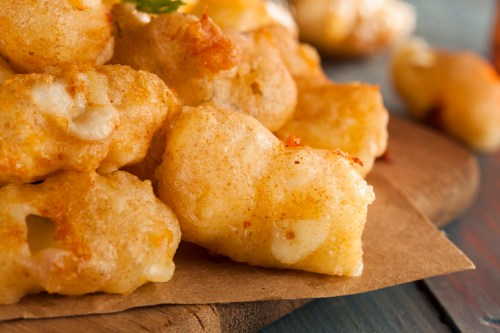 Close-up of golden, crispy fried cheese curds on a wooden surface, garnished with herbs.