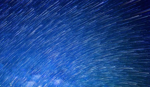 A night sky filled with streaks of stars, creating a dynamic, swirling effect against a deep blue backdrop.