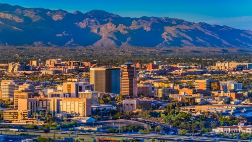 A panoramic view of a city skyline with mountains in the background during sunset.