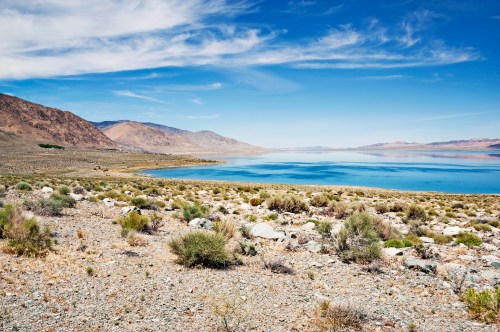 A serene landscape featuring a calm blue lake surrounded by rocky terrain and distant mountains under a clear sky.