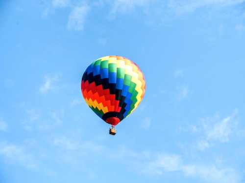 A colorful hot air balloon floats against a clear blue sky with a few clouds.