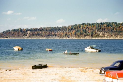 A serene lake scene with several boats on the water and a colorful tree line in the background under a clear sky.