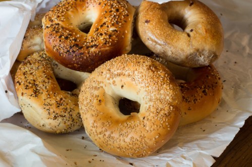 A variety of freshly baked bagels, including sesame and poppy seed, arranged on crumpled white paper.
