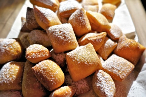 A pile of golden, powdered sugar-dusted pastries arranged on a white surface.