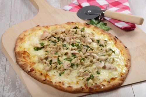 A freshly baked pizza topped with chicken, herbs, and melted cheese on a wooden pizza peel.