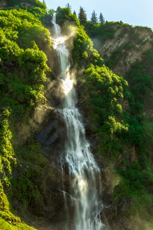A majestic waterfall cascading down a lush, green mountainside, surrounded by mist and sunlight.