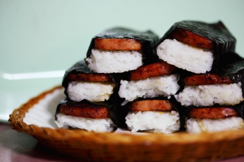 A plate of stacked sushi rolls made with rice and slices of spam, wrapped in seaweed.