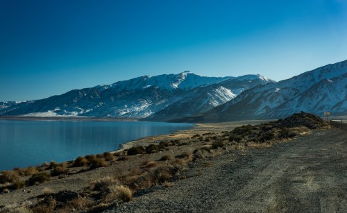 A serene landscape featuring snow-capped mountains beside a calm lake under a clear blue sky.