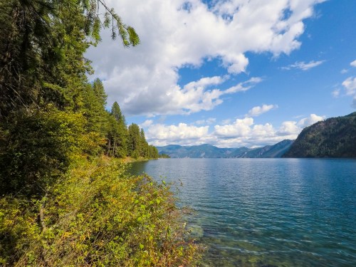 A serene lake surrounded by lush greenery and mountains under a partly cloudy sky.