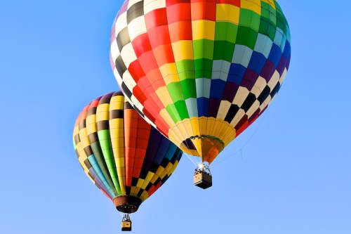 Two colorful hot air balloons ascend against a clear blue sky.