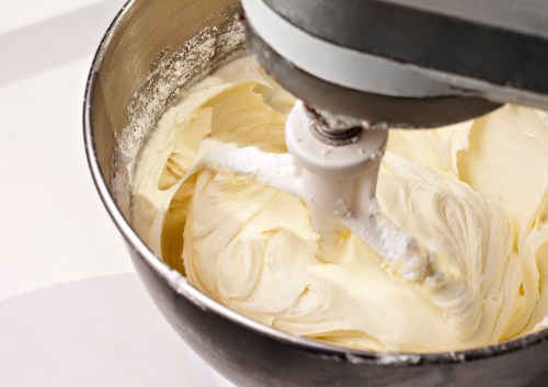 A close-up of a mixing bowl with creamy batter being mixed by an electric mixer.