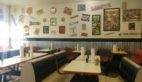 A diner interior with red and black booths, tables, and a wall decorated with vintage signs and posters.