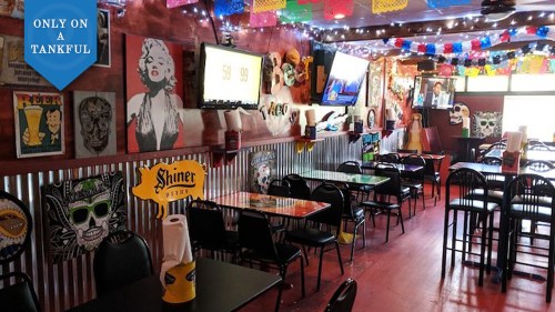 Colorful restaurant interior with tables, vibrant decor, and TVs, featuring a lively atmosphere and festive lighting.