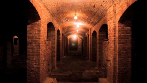 A dimly lit brick corridor with arched openings and hanging lights, creating an eerie atmosphere.
