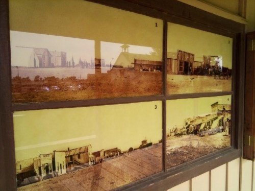 Four historical photographs displayed in a window, showcasing old buildings and landscapes from a bygone era.