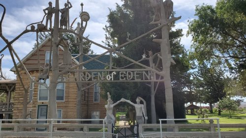 A wooden sign reading "Garden of Eden" with sculptures of figures and trees in a park setting.